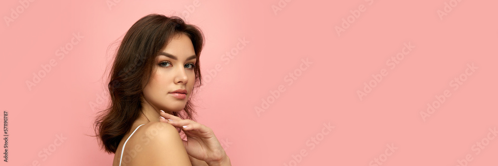 Naklejka premium Closeup portrait of young beautiful girl with long dark hair looking at camera over pink background. Concept of beauty, skin care, cosmetology, wellness, makeup