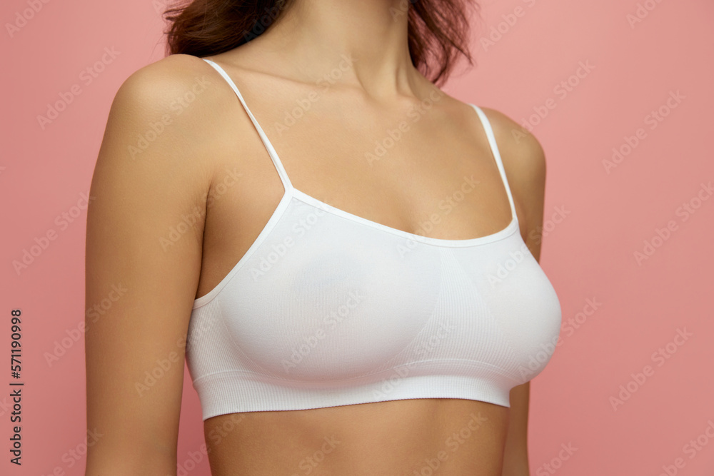 Fototapeta premium Cropped image of female body, breast in white underwear isolated over pink studio background. Mammoplasty, health, beauty and fashion