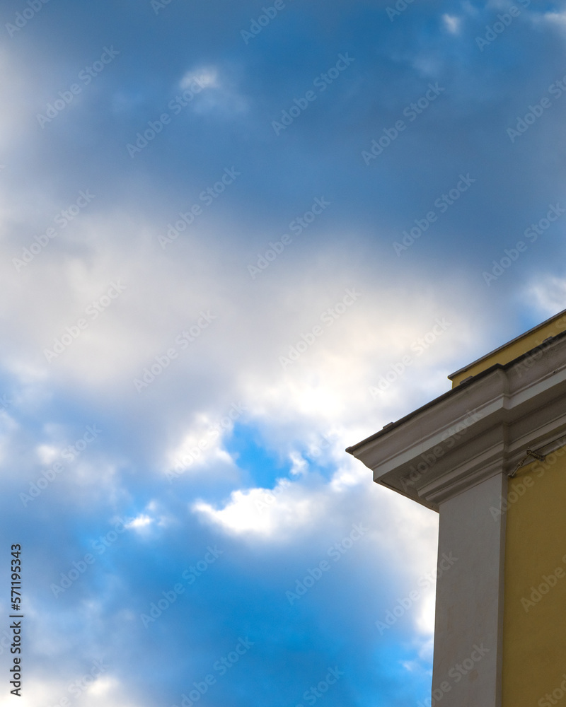 Cloudy background, angular building, poor and minimal art. White and blue clouds with an edge of a white and orange building.