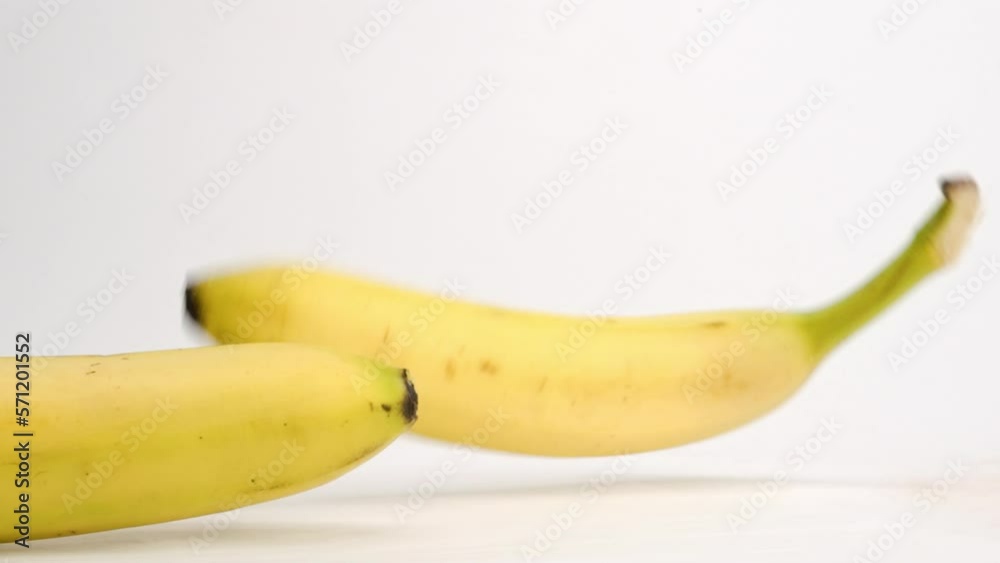 Whole, individual ripe yellow bananas falling onto white table top and bouncing around in slow motion Whole, individual ripe yellow bananas falling onto white table top and bouncing around in slow motion