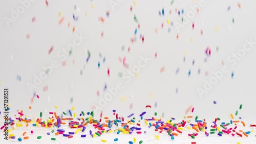 Birthday party celebration rainbow sprinkles raining down and bouncing off white table top in slow motion photo
