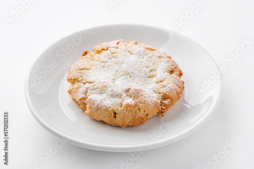 One freshly baked cookie with powdered sugar on a white plate on the table. Homemade cakes for breakfast.