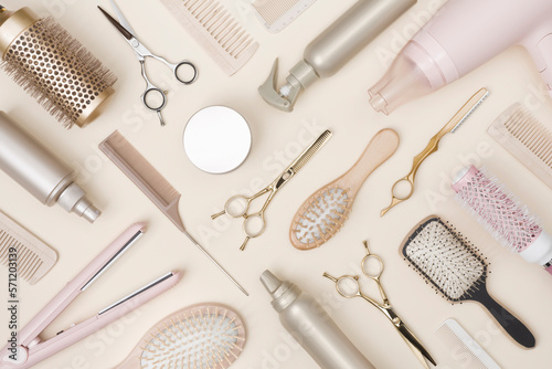 Hairdressing tools and various hairbrushes on cream background top view