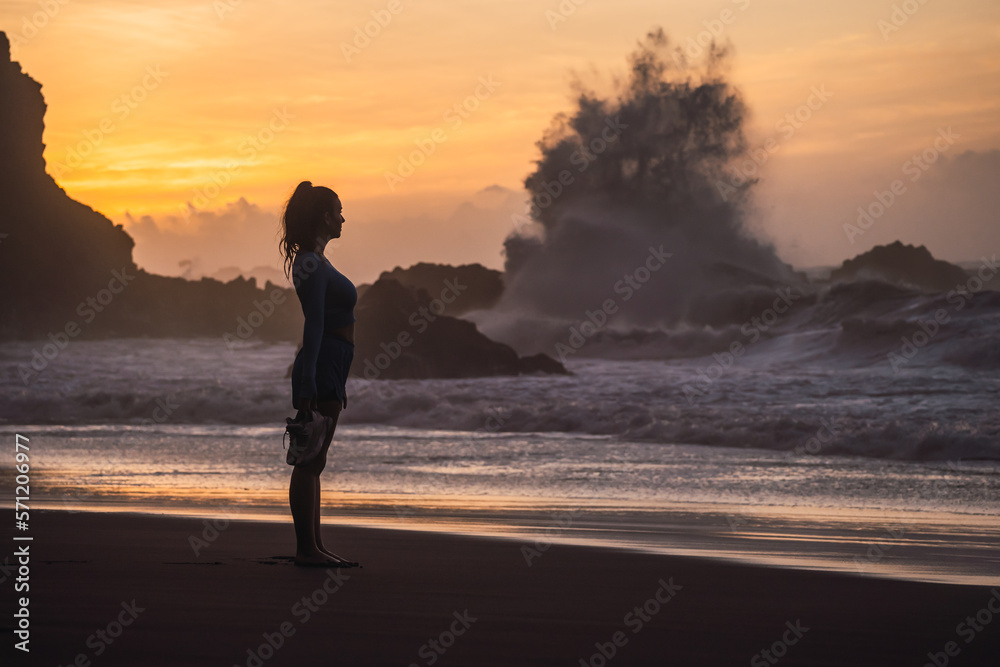 woman walking on the beach with her shoes in her hand while looking at the sea. sunset on the island of tenerife Spain
