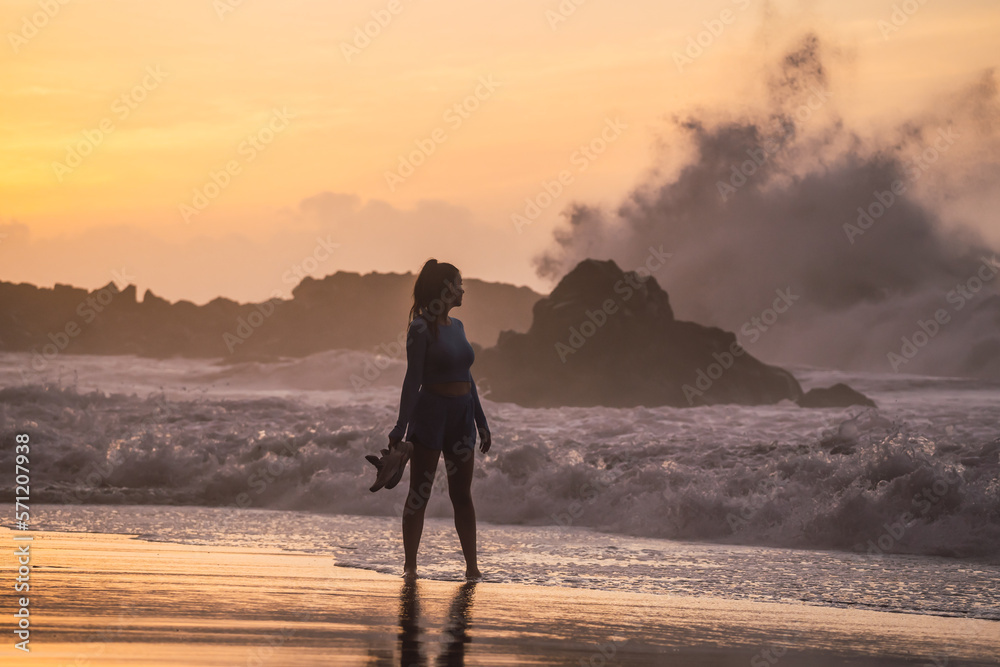 woman walking on the beach with her shoes in her hand while looking at the sea. sunset on the island of tenerife Spain