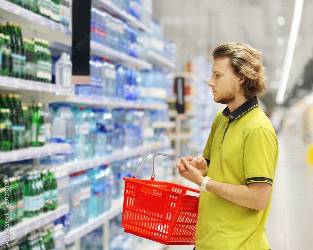 Young man shopping in supermarket, reading product information,supermarket shelves with water bottles