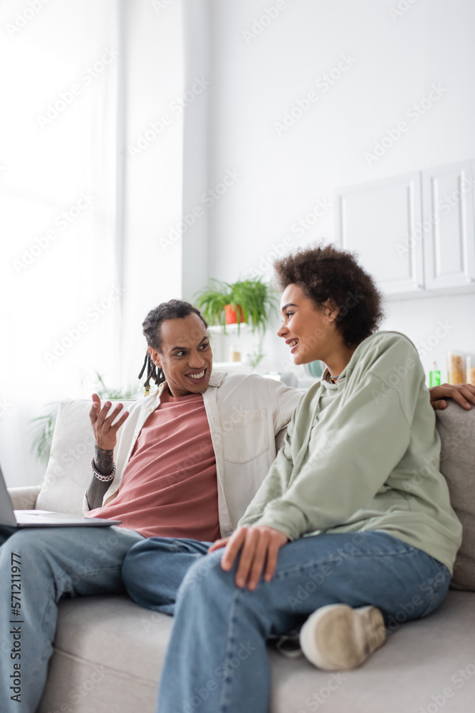 African american couple talking near laptop on couch at home. African american couple talking near laptop on couch at home.