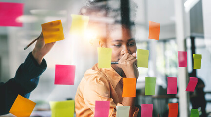 Young businesswoman creative team using sticky notes in glass wall to writing strategy business plan to development grow to success.