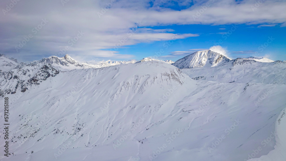 Panoramic view of austrian alps in Winter. High peaks covered with snow and clouds on a sunny winter day.