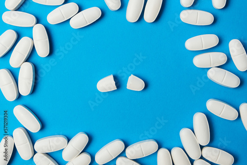 A pill broken in two, surrounded by other pills. Top view on a blue background.