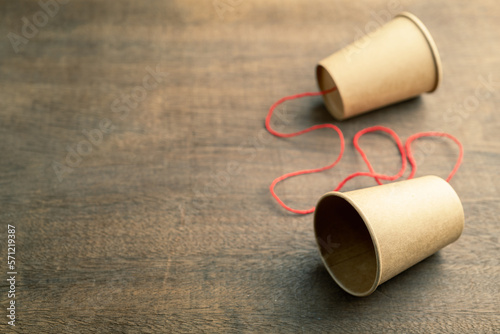 Old style cup phone, two brown paper cups with red string, on wood background, two way communication photo