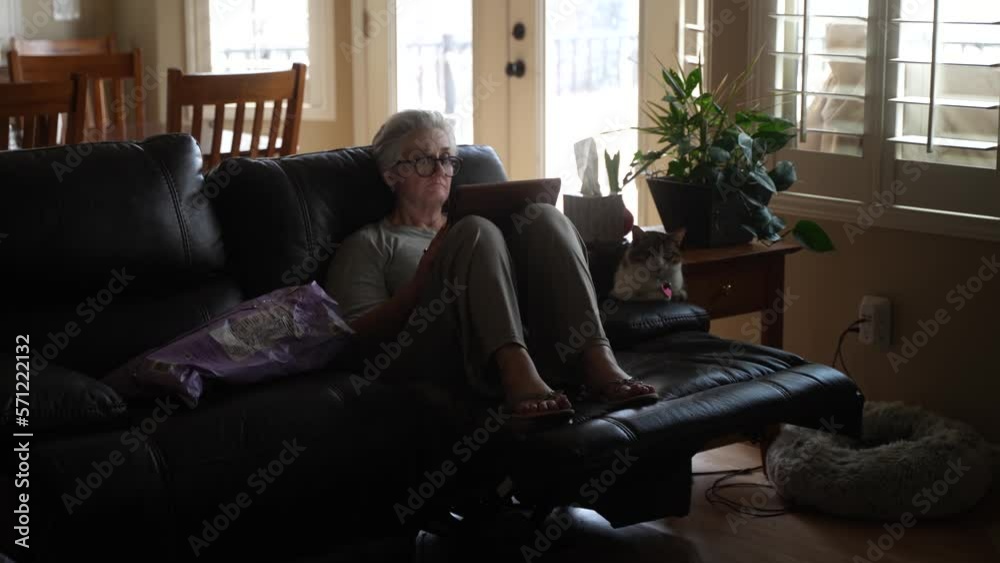 Senior woman reading on a tablet next to her cat while it snows outside Senior woman reading on a tablet next to her cat while it snows outside