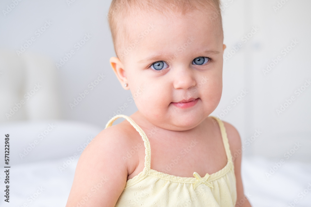 portrait of cute smiling baby girl in yellow bodysuit on white bedding. Healthy newborn child