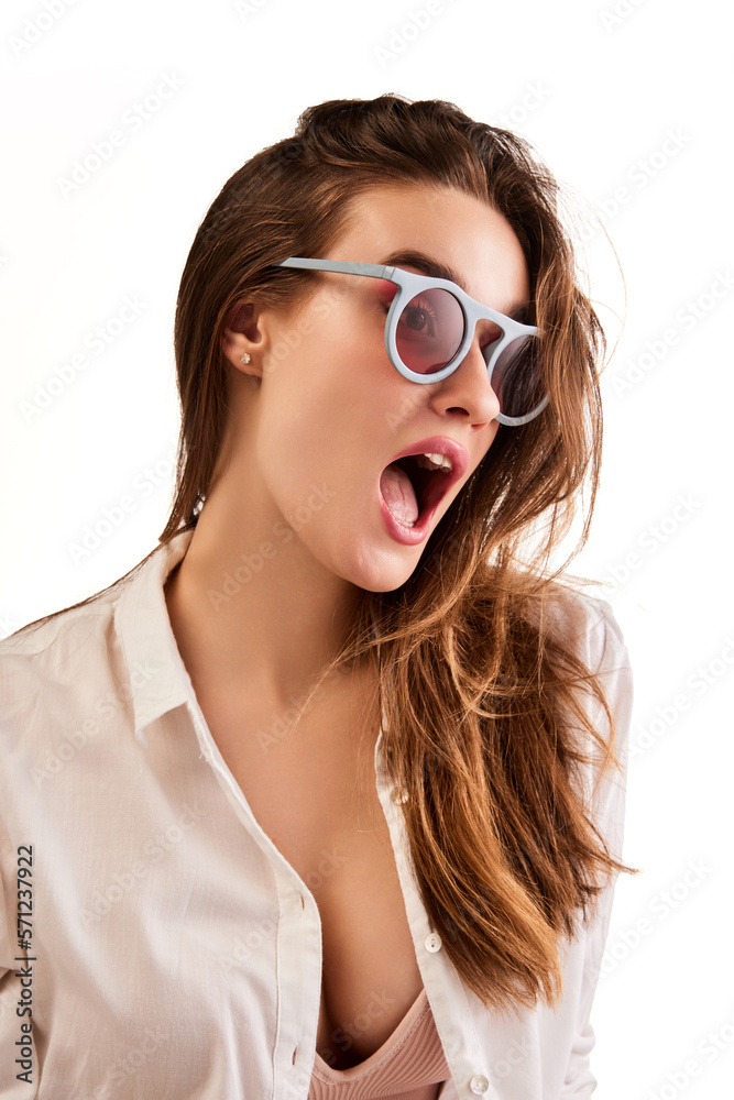 Portrait of young beautiful woman in stylish clothes and trendy sunglasses posing against white studio background. Concept of natural beauty, youth, health, wellness, femininity, make-up, fashion Portrait of young beautiful woman in stylish clothes and trendy sunglasses posing against white studio background. Concept of natural beauty, youth, health, wellness, femininity, make-up, fashion