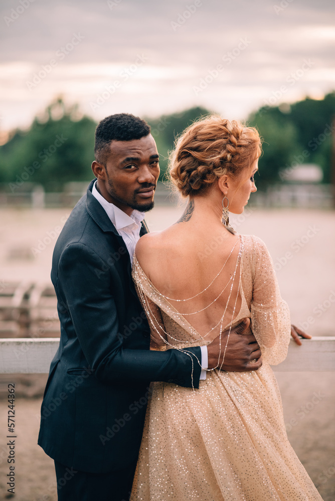 Two lovers black man and white woman stand embracing on a ranch at sunset Two lovers black man and white woman stand embracing on a ranch at sunset