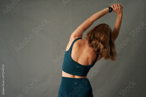 Rear view of young caucasian woman in sports clothing with arms raised while stretching in studio