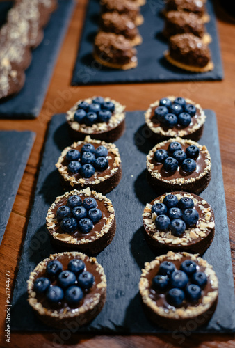 Delicious tartlets with chocolate and fresh blueberries, close-up. A refined European dessert. Showcase of a pastry shop with desserts