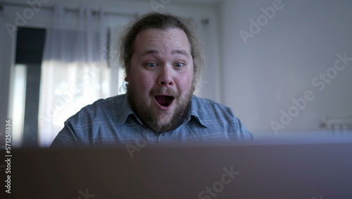 One happy man celebrates success in front of computer. A male chubby entrepreneur kissing laptop screen overjoyed by excellent news