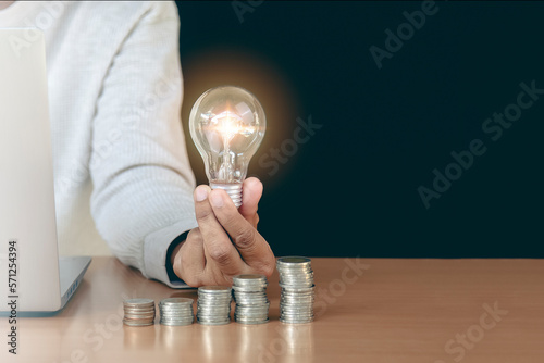 Woman holding light bulb in hand on wooden table in concept of savings, investment, savings and accumulation plan