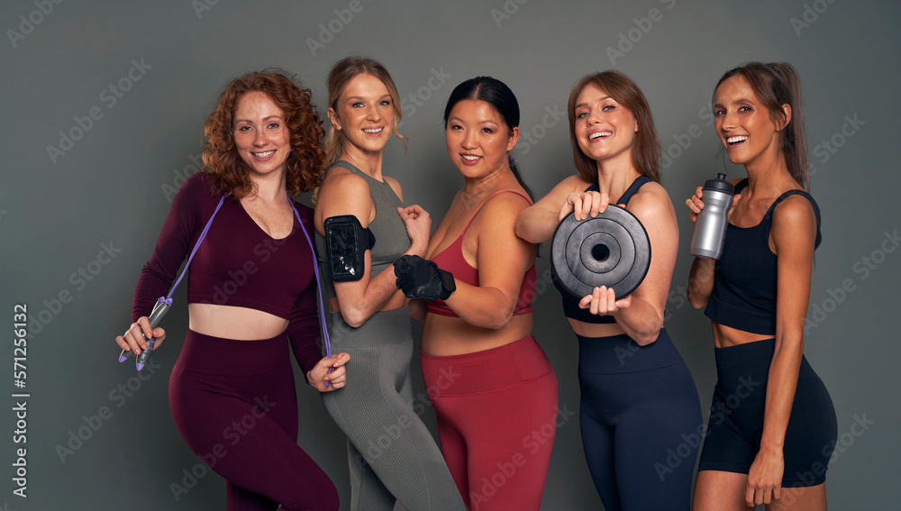 Five young women in sports clothes and gym accessories in studio