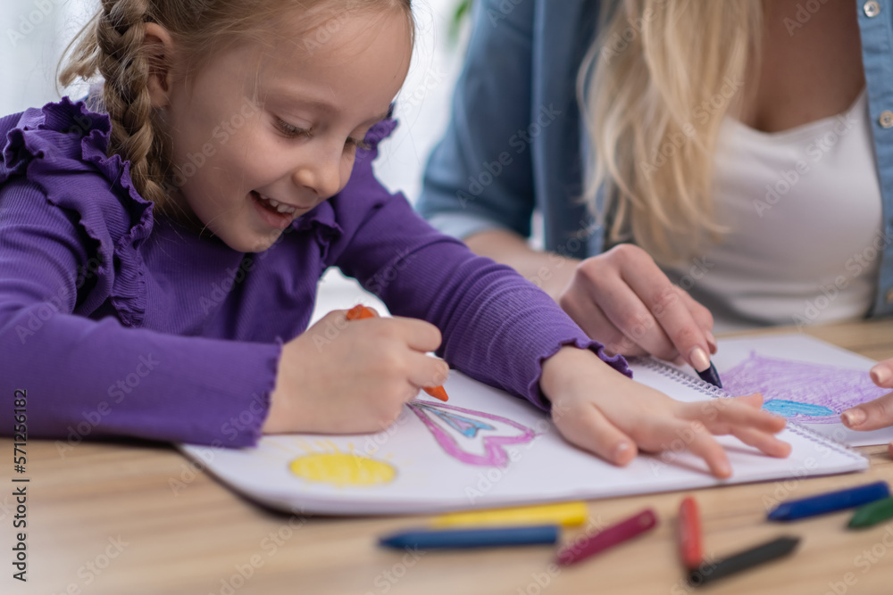 Close up portrait of little girl painting with her mother on table using different colours pensil and crayons smiling having fun learning drawing Close up portrait of little girl painting with her mother on table using different colours pensil and crayons smiling having fun learning drawing