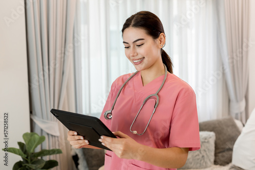 Young processional Caucasian Geriatric doctor in pink scrubs with stethoscope holding digital tablet. Physician in hospital nursing or wellbeing county. Happy caregiver taking care of elderly people.