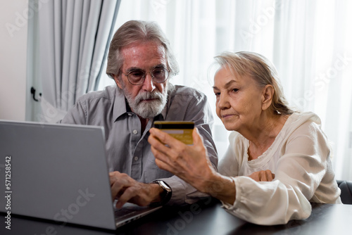 Happy Caucasian 70s mature couple using credit bank card and laptop transferring money purchases online shopping. Senior man and woman surfing the internet. Modern retired lifestyle people. © butsaya33