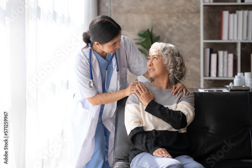 Asian female doctor or nurse gently guide and care for elderly patient at home, giving warm encouragement and consolation.