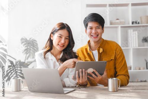 Asian couple husband and wife using laptop and paper bills at home use banking applications sit together at the table A cautious family spouse is confused by high expenses. insurance or rent concept