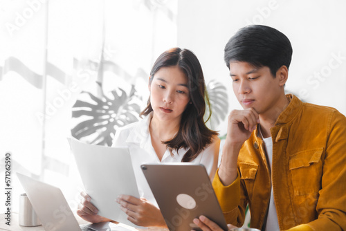 Asian couple husband and wife using laptop and paper bills at home use banking applications sit together at the table A cautious family spouse is confused by high expenses. insurance or rent concept