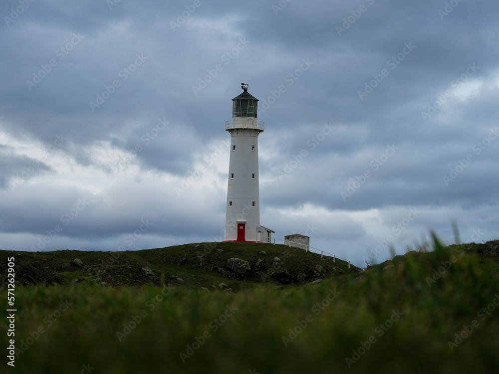 Low angle green grass shot of tall white Cape Egmont Lighthouse on cloudy day in South Taranaki North Island New Zealand