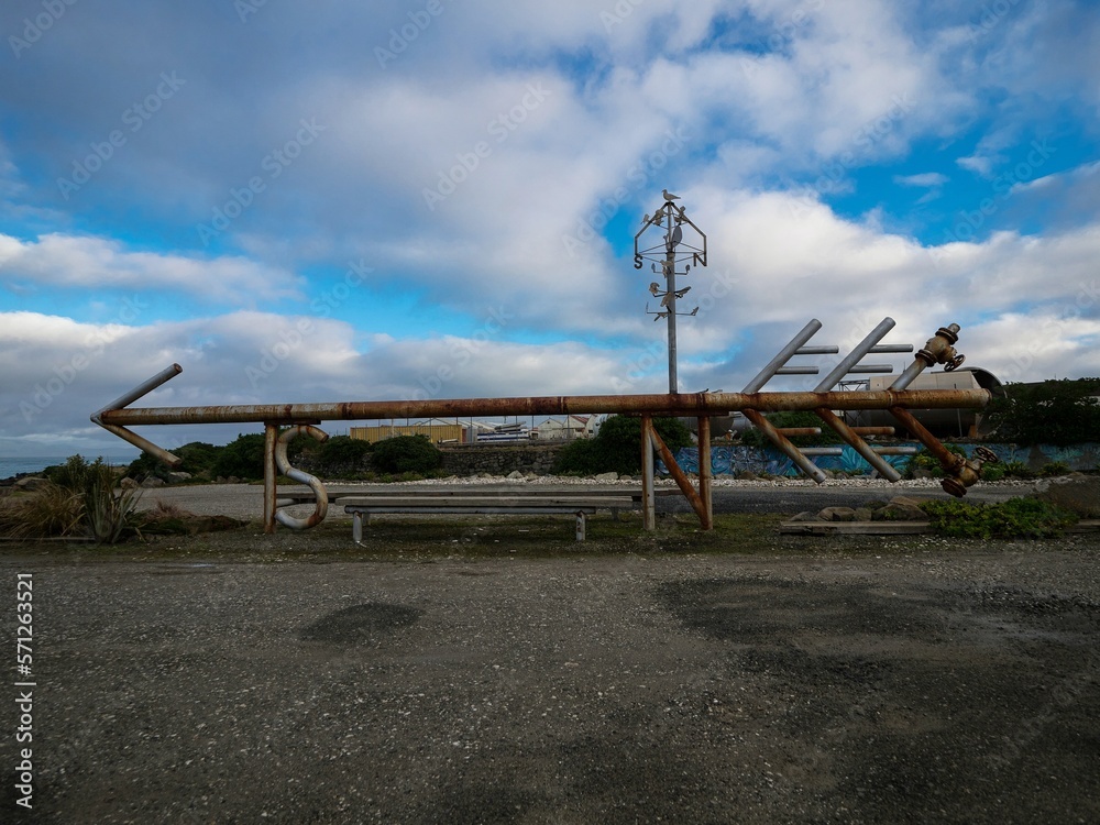 Old rusty pipe arrow shaped industrial art sculpture, navigation direction symbol in gravel car park, Bluff New Zealand Old rusty pipe arrow shaped industrial art sculpture, navigation direction symbol in gravel car park, Bluff New Zealand