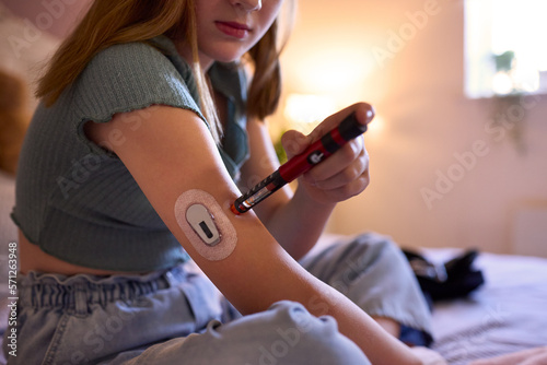 Close Up Of Young Diabetic Girl Sitting On Bed In Bedroom At Home Using Kit To Check Insulin Levels photo