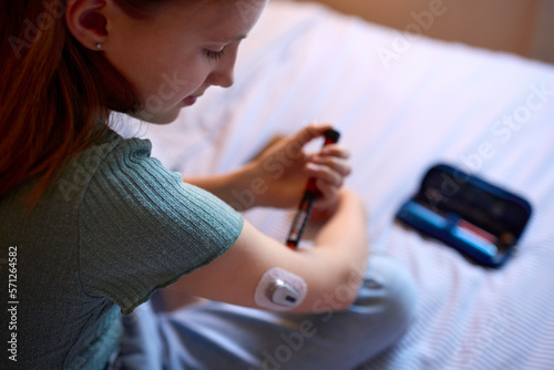 Close Up Of Diabetic Girl On Bed In At Home Using Insulin Pen To Measure To Check Blood Sugar Level photo