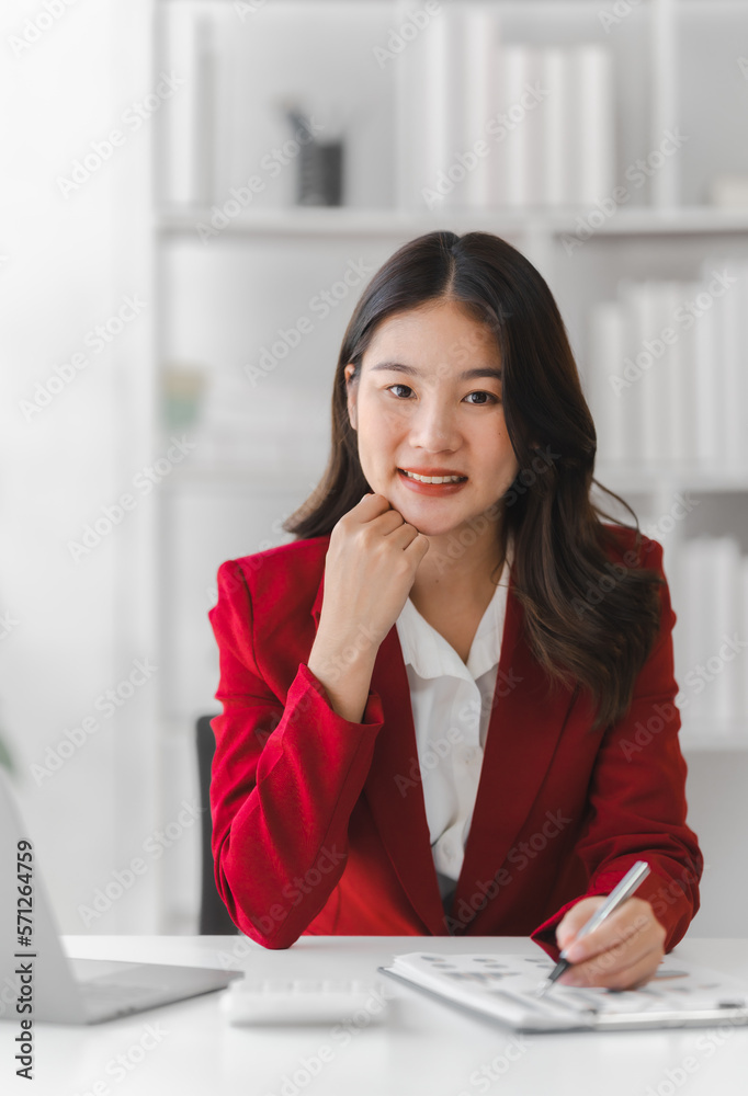 Attractive pretty asia businesswoman wearing red formal suit working with balance sheet, doing math in financial contract of company, Looking at camera Attractive pretty asia businesswoman wearing red formal suit working with balance sheet, doing math in financial contract of company, Looking at camera
