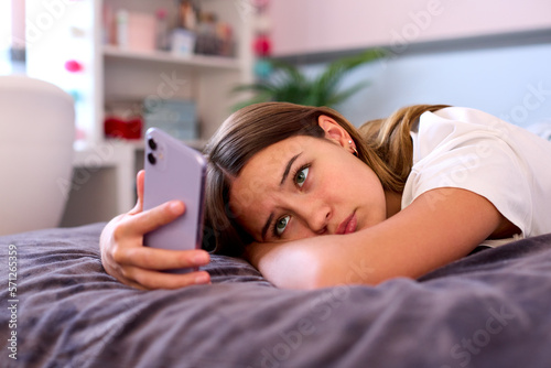 Depressed Teenage Girl Lying On Bed At Home Looking At Mobile Phone photo