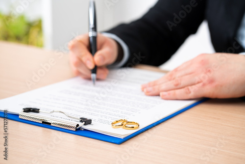 Close-up of wife signing divorce document with wedding rings over it at home