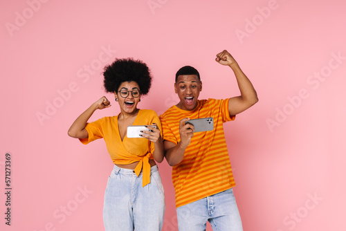 Afro couple screaming and showing winning gesture while playing online game on mobile phones isolated