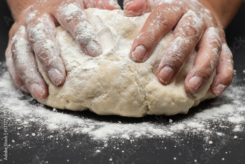 hands kneading bread dough on black table