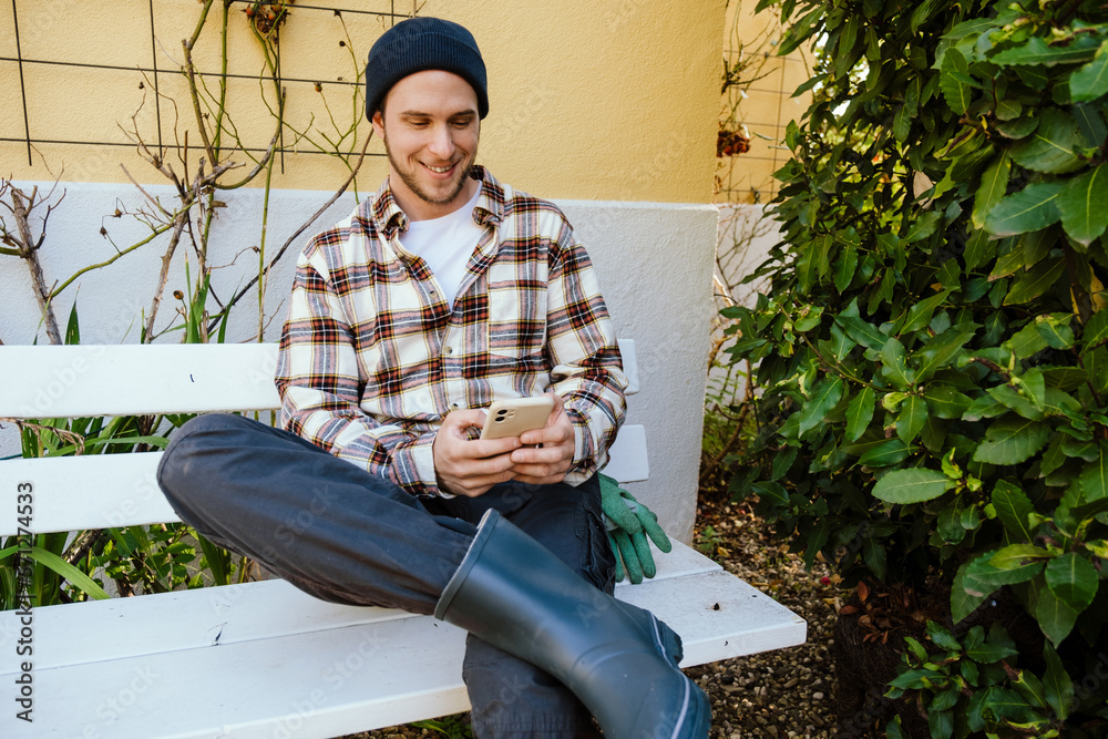 Obraz premium Smiling man gardener using mobile phone while sitting on bench