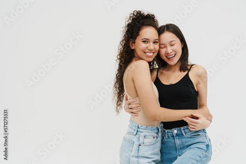 Beautiful multinational girls smiling and hugging while standing over isolated white background