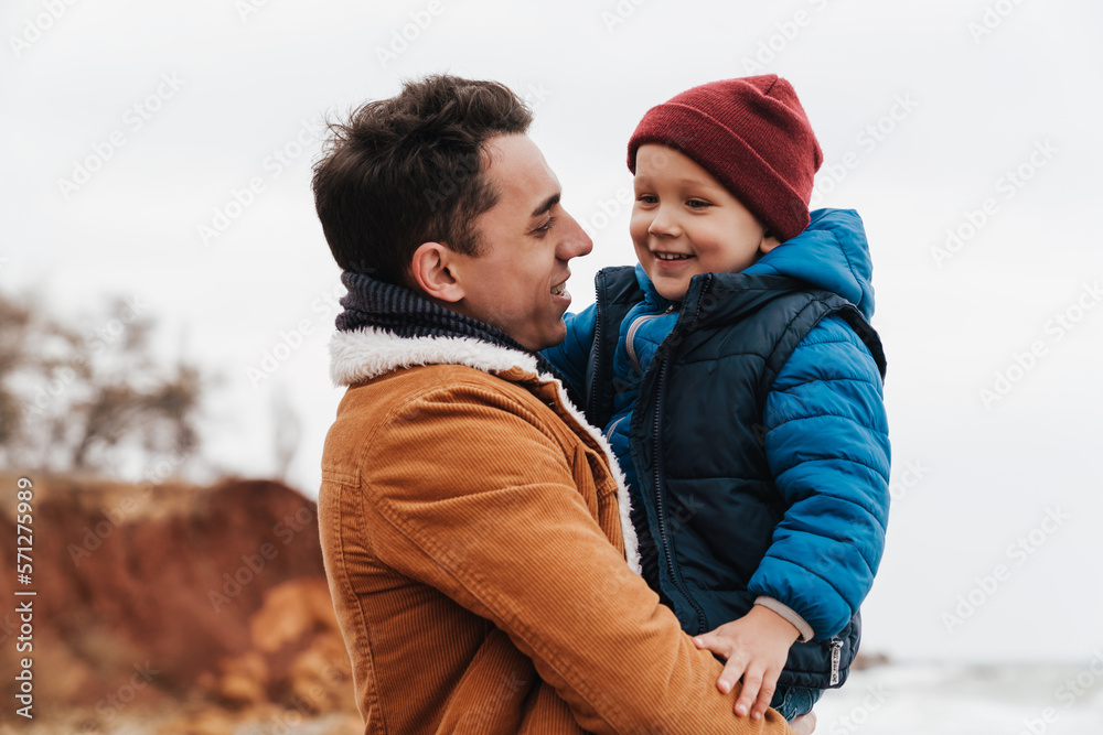 Fototapeta premium Smiling father holding son in his arms while spending fun time together on beach