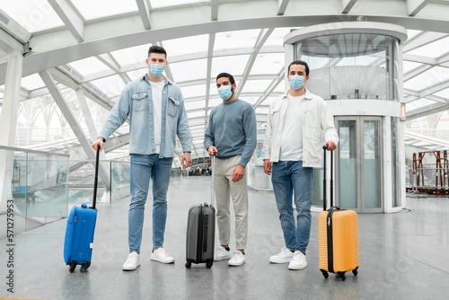 Three Tourists Guys Wearing Face Masks Standing In Modern Airport