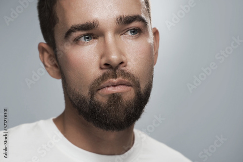 Young and handsome bearded man with clean skin against gray background