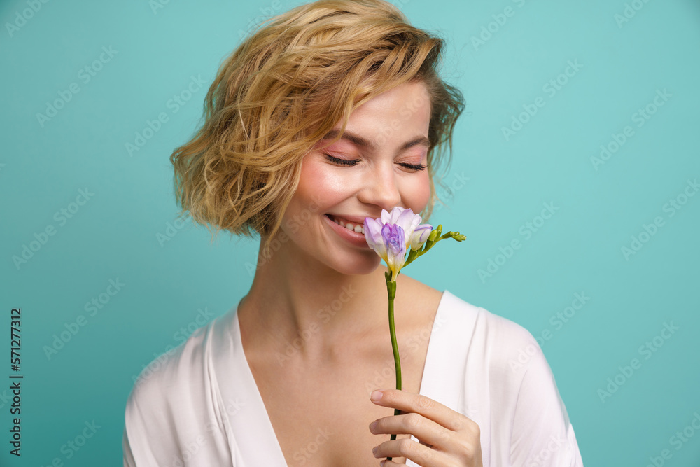 ?heerful woman smelling freesia flower isolated over blue background ?heerful woman smelling freesia flower isolated over blue background