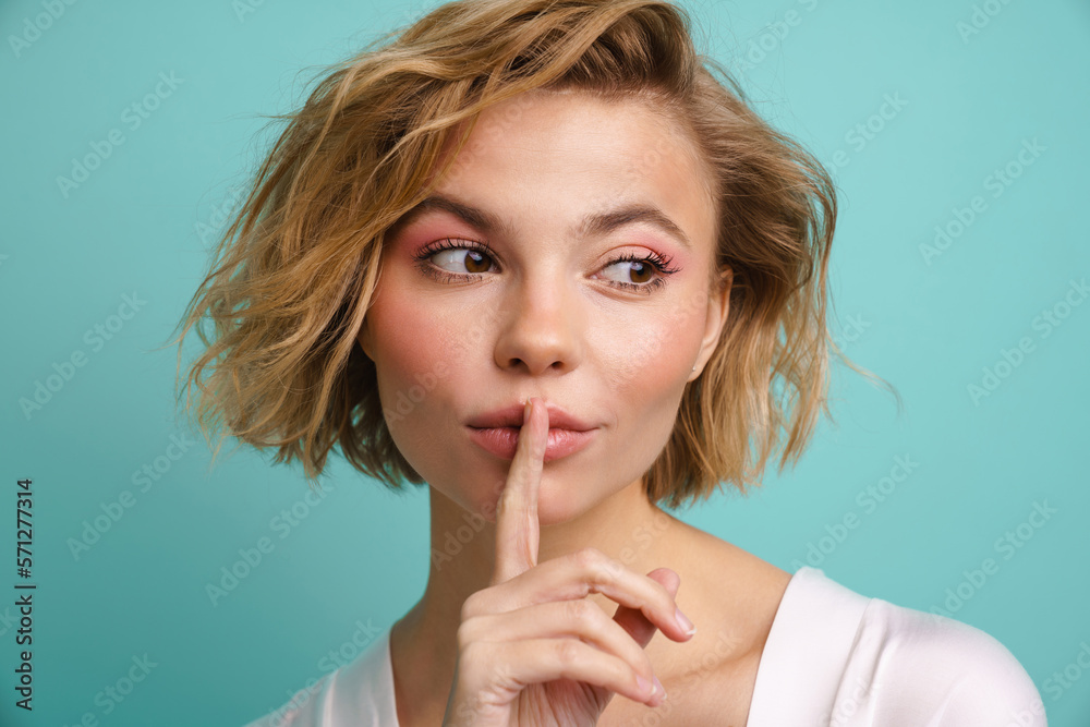Beautiful woman showing silence gesture and looking aside while standing isolated