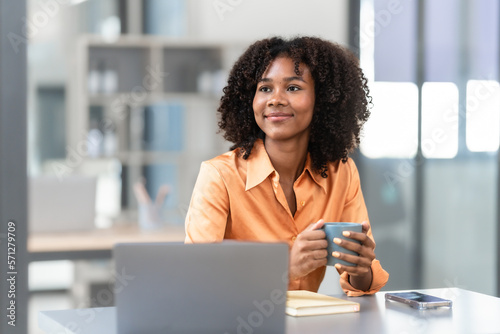Using laptop computer, Young pretty african american business woman bookkeepers working with balance sheet yearly reports to calculate tax and online consult in modern office.