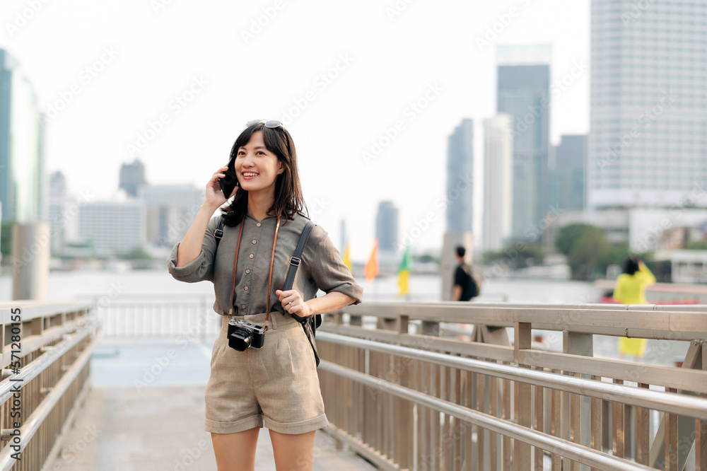 Young Asian woman backpack traveler using mobile phone in express boat pier on Chao Phraya River in Bangkok. Journey trip lifestyle, world travel explorer or Asia summer tourism concept