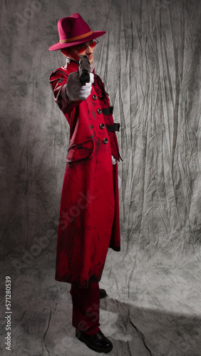 A stylish guy in a vampire costume, a red hat, a coat and tinted glasses. aiming a gun