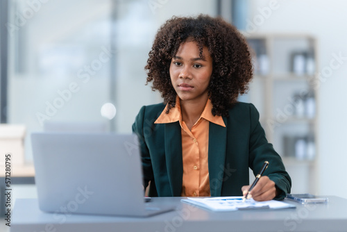 Online consult with laptop, video conference, Young pretty african american business woman bookkeepers working with balance sheet yearly reports to calculate tax and online consult in modern office.